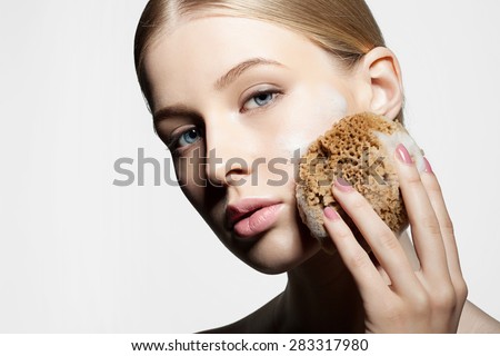 Woman cleans and exfoliates the skin with a natural sponge foam face on a white background