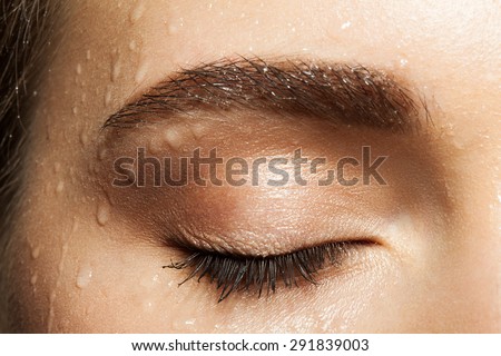 Close-up of closed eye with long eyelashes and eyebrows brown with water drops