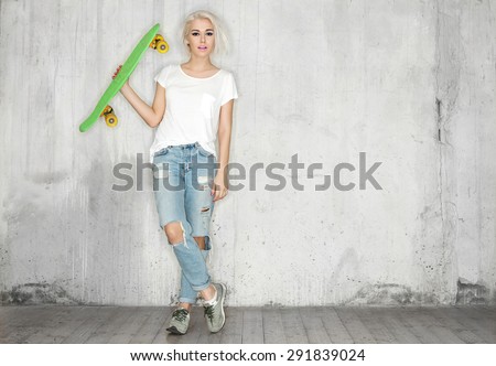 Girl with a skateboard in his hand against the background of a concrete wall