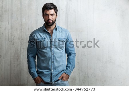 Portrait of a brutal Man in jeans standing against a cement wall