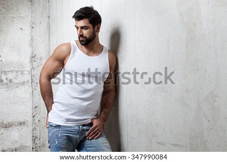 Brutal man in a white T-shirt and jeans standing on the cement wall background