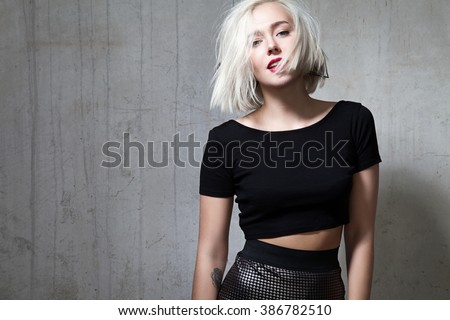 Fashionable girl with red lipstick and short hair and dressed in a black T-shirt, standing on the cement wall background