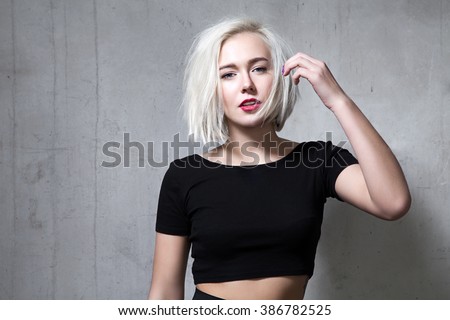 Portrait of a fashion blonde with short hair and wearing a black T-shirt on the background of a cement wall