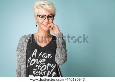 Fashionable girl with glasses and short hair and dressed in a gray T-shirt, standing on the blue background