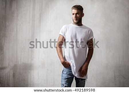 Handsome bearded man in white blank t-shirt standing on the cement wall background