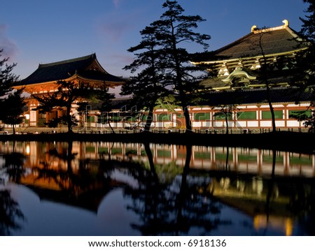 Illuminated evening view of the inner gate and wall surrounding Todai-ji temple with a pond in the foreground in Nara, Japan.  Todai-ji temple can be seen in the background behind the wall.