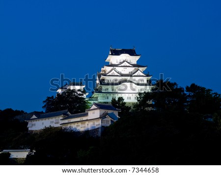 Night time view of the main tower and some of the inner walls of Himeji Castle lit up on the hillside with dark shapes of the trees of the castle grounds around the base of the hill