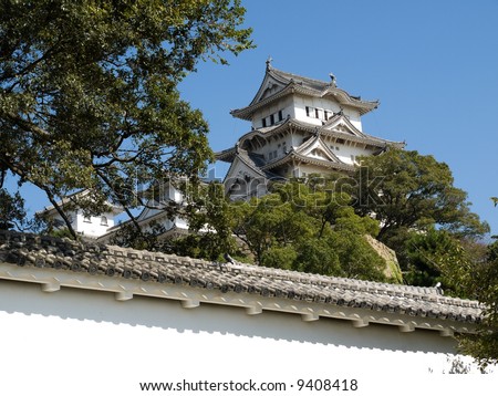 Glimpse of the main tower of Himeji Castle in the distance behind one of the lower walls  and trees of the castle grounds during the daytime