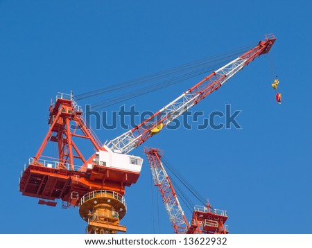 Red and white steel crane at a high rise building site in the city with a blue sky background