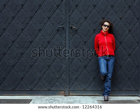 woman in red and blue clothes stands against a dark gate