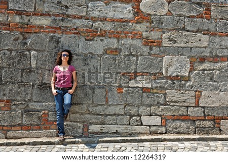 woman in red and blue clothes stands against a stone wall