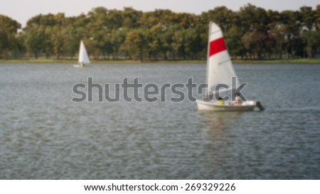 blurry landscape with people sailing in the lake at sunrise useful as background