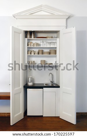 Kitchen cabinet with fridge, water tap and dishes.
