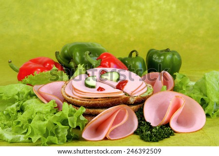 Set of food components on greenish background: ham, bread, paprika, lettuce.