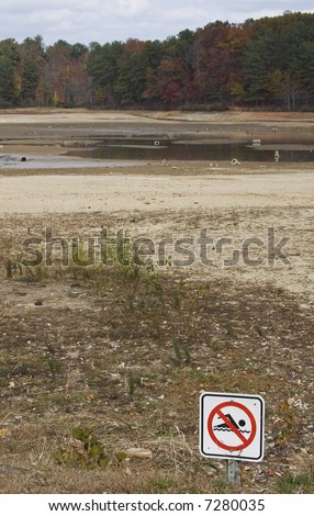A no swimming sign in front of a dried up drought stricken lake.  Focus on the sign.