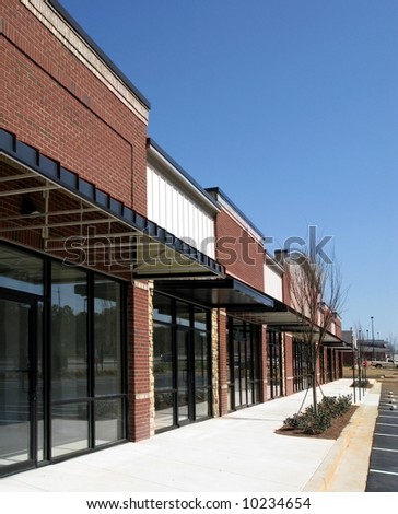 A suburban shopping center made of textured brick, stone, and glass in the final stage of construction.