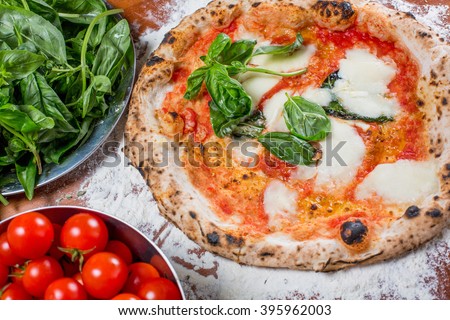 Traditional italian pizza with mozzarella, tomato and basil, on a wooden table with the ingredients