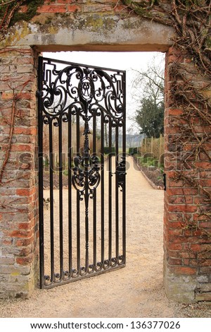 A cast iron garden gate standing half open, leading to a garden beyond.