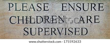 A carved wooden sign warning that children should be supervised in the area