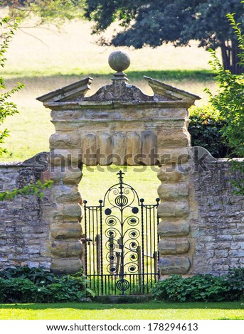 An ornate ironwork gate set into a decorative wall leading from a sheltered garden into an extensive parkland
