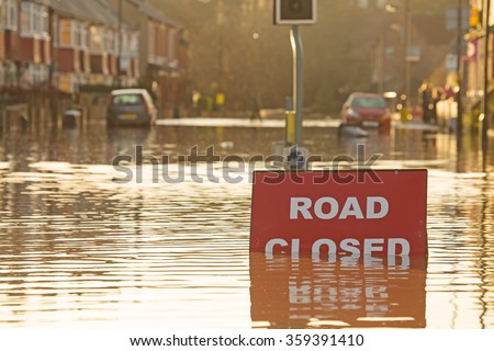 A \'Road Closed\' sign partially covered in flood water lit by the evening sun
