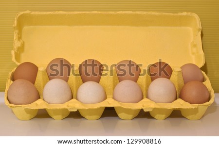 A dozen white and brown eggs in a yellow egg box