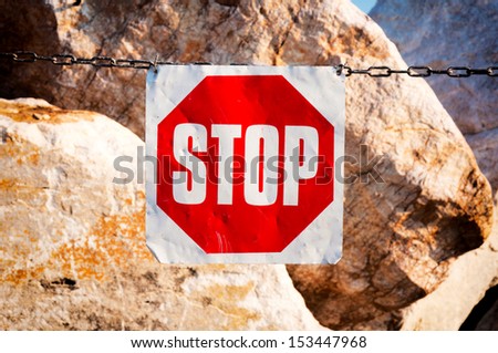 Metal stop sign on the chain with stones in background