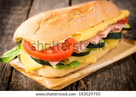 Big sandwich stuffed with ham,cheese and vegetables on the wooden table