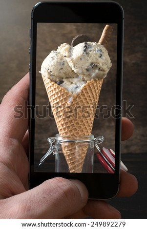 Ice cream with cookies in jar on wooden background photographing with camera od mobile phone
