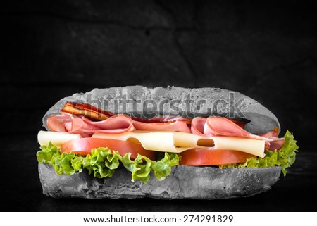 Big ciabatta sandwich with meat and cheese on dark background,selective color
