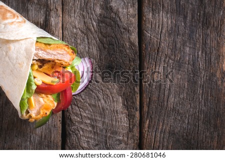 Tortilla chicken wrap sandwich on wooden background with blank space