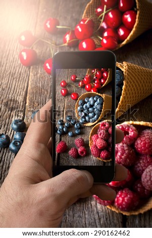 Man photographing fruits in ice cream cone with his cellphone camera,selective focus