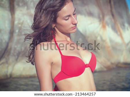 Young woman outdoor portrait on wild rocky seashore beach stone landscape sea view in red bikini swimsuit