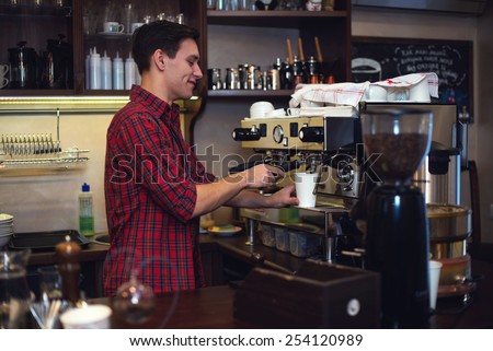 Young handsome barista hipster making coffee for his clients in the cafe