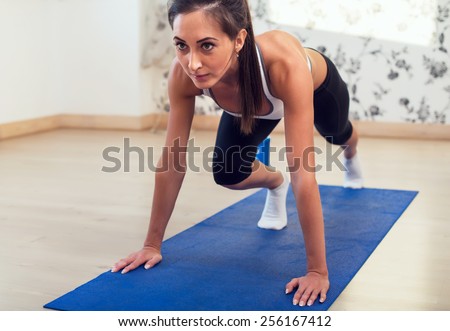 Young determined confident slim woman doing exercises on the blue mat looking straight forward