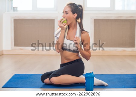 Caucasian beautiful healthy athletic sportive girl eat green apple and Yoga Mat shaker after the training and looking at camera