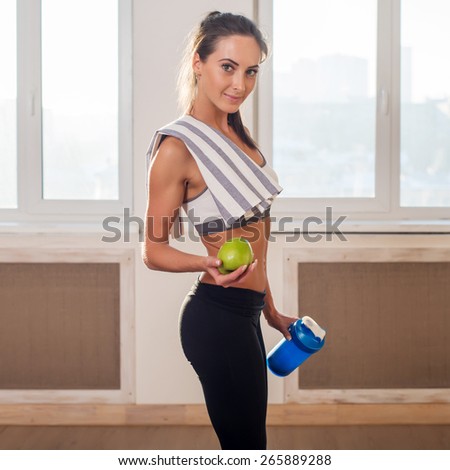 Gorgeous young athletic sportive woman in sport outfit holding apple and blue shaker after the training