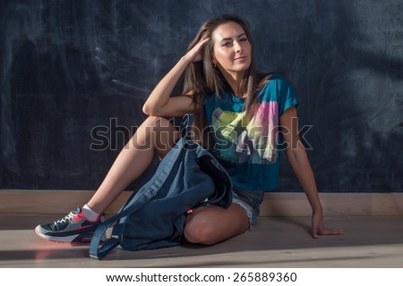 Trendy Hipster Girl in jeans shorts and t-shirt Sitting on the floor looking at the camera.