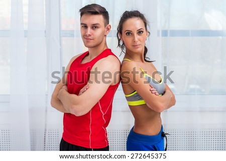 athletic sporty couple friends woman and man trainers or coach and client in sport hall gym standing back to back sportsmen professionals looking at camera.