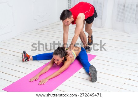 Active sporty woman doing stretching exercises aerobics or warming up wide legged tilt to forward for flexibility with the help training mate trainer.
