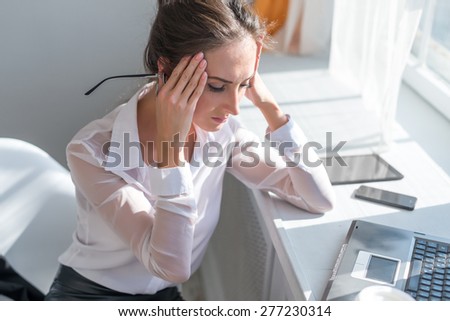 Portrait of tired young business woman suffering from headache in front of laptop at office desk.