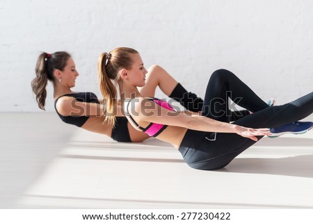 Two sporty women doing exercise abdominal crunches, pumping a press on floor in gym concept training exercising workout fitness aerobic side view.