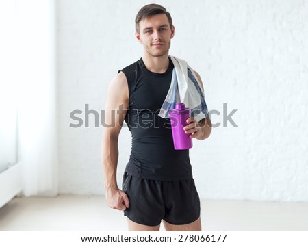 Portrait of a athletic man after doing exercises sportsman holding towel and shaker protein cocktail or bottle with water