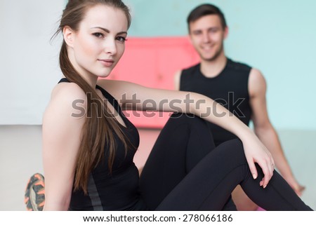 sporty couple friends slim athletic woman and man trainers team or coach client in sport gym sitting at floor sportsmen professionals looking at camera.