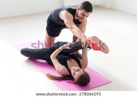 woman lying on mat lifting leg up doind exercise for flexible male trainer helping her concept sport health fitness aerobics gymnastic.