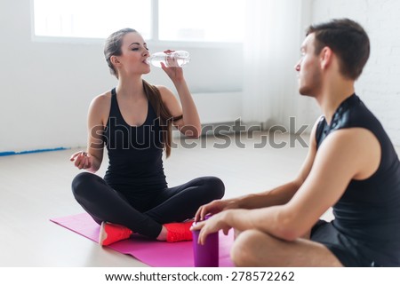 Sport connecting people friends relaxing after workout girl drinking water and man Side view of young couple in sports clothing sitting face to face and talking conversing