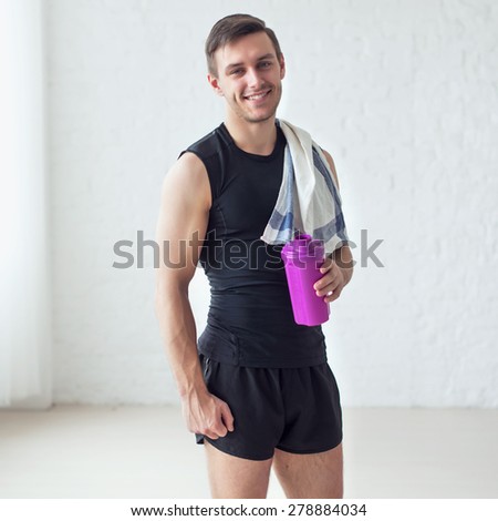 Portrait of a athletic smiling man after doing exercises sportsman holding towel and shaker protein cocktail or bottle with water