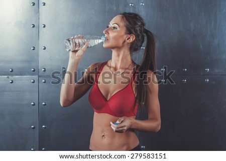 Muscular sporty athlete woman drinking water at the gym after exercising working out fitness, sport, training and lifestyle concept