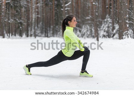 Fitness young woman stretching her legs outdoors Winter park forest