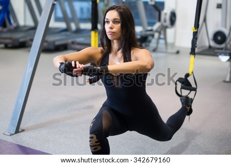 Athletic woman workout out squats weighted lunges exercise for butt legs with suspension straps in fitness club or gym